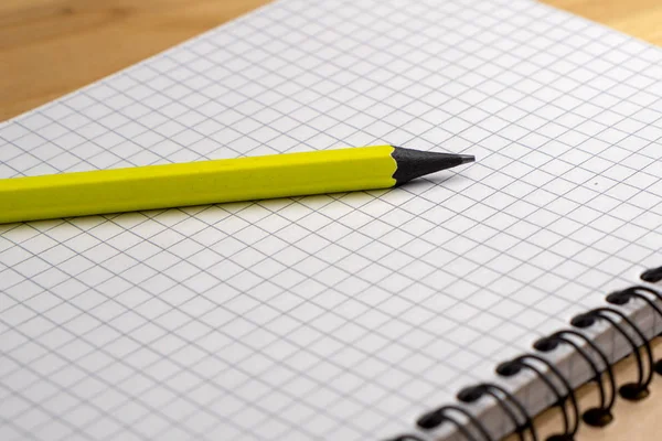 Yellow pencil on a notebook with sheets in a cage on a wooden table. Concept for shopping list, notes, planning. Side view — Stock Photo, Image