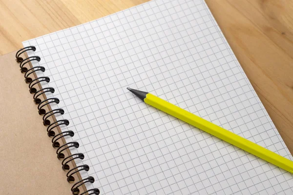 Yellow pencil on a notebook with sheets in a cage on a wooden table. Concept for shopping list, notes, planning. Top view — Stock Photo, Image