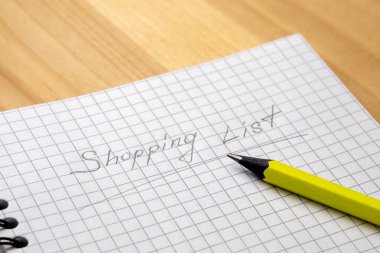 Ahşap bir masada bir kafeste çarşaf ile bir defter üzerinde sarı kalem. Alışveriş listesini imzala