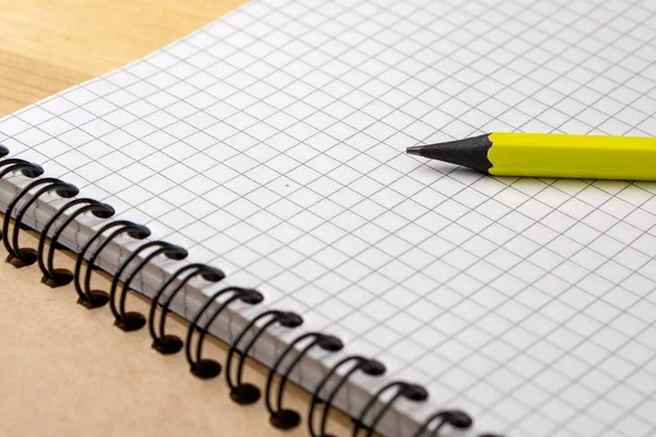 Geel potlood op een notitieboekje met vellen in een kooi op een houten tafel. Concept voor boodschappenlijstje, notities, planning. Zijaanzicht Rechtenvrije Stockafbeeldingen
