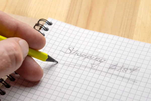 A man writes in yellow pencil in a notebook. Sign Shopping List. Close-up — Stock Photo, Image