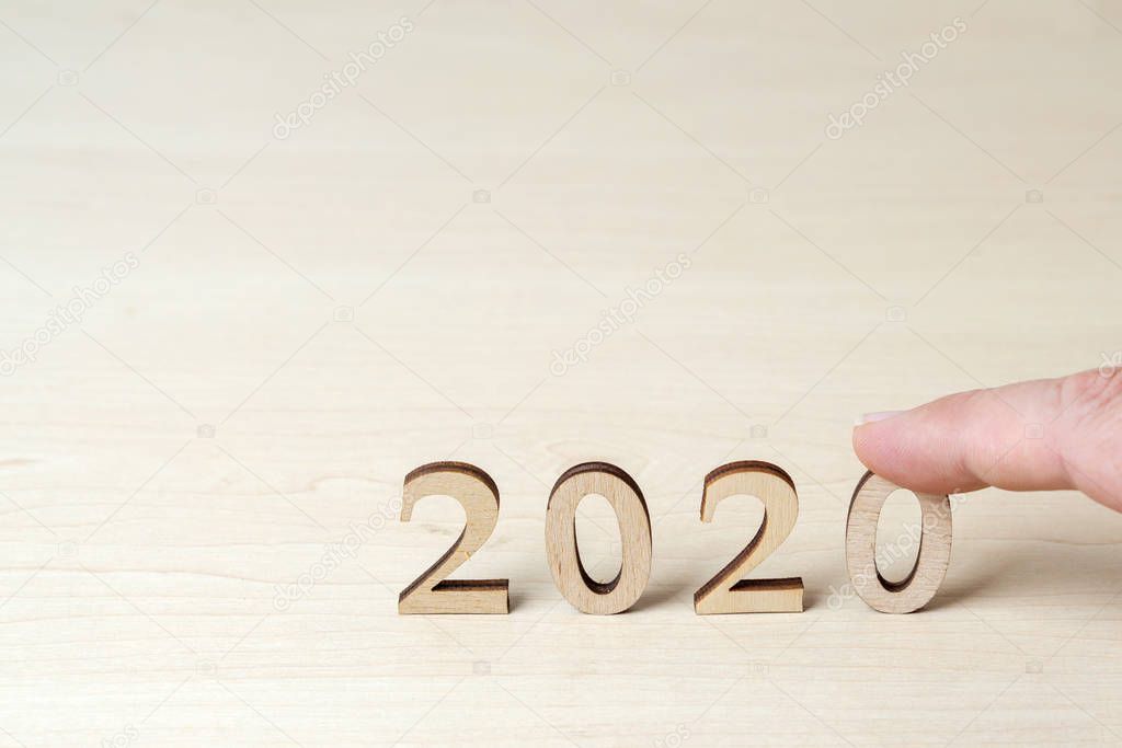 Hand sets wooden numbers on the table, symbolizing 2020 new year