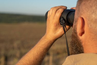Sakallı bir adam dürbünle yakından bakar. Avcı aramak için dürbün kullanır.