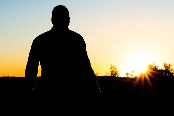 Silhouet van een man met een wapen in zijn handen op een zonsondergang achtergrond — Stockfoto