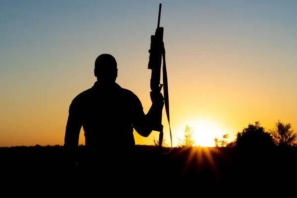 Silhouet van een man met een wapen in zijn handen op een zonsondergang achtergrond — Stockfoto