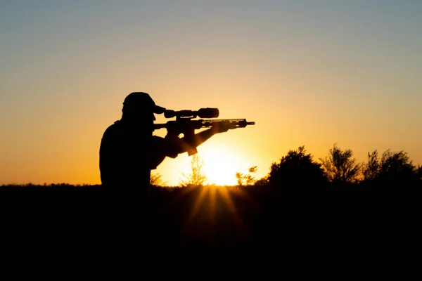 Silueta muže se zbraní v rukou na pozadí západu slunce — Stock fotografie