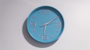 Beyaz bir duvar üzerinde mavi bir saat zaman atlamalı. Saat işliyor, 5 ve 12 ucunda başlar.