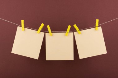 notlar ve hatırlatmalar için sarı not defteri kağıt levhalar, kahverengi bir arka plan üzerinde bir ip asılı dekoratif sarı clothespins ile sabitlenmiş