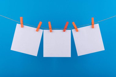 notlar ve dekoratif turuncu clothespins ile sabitlenmiş beyaz renk hatırlatmalar için not defteri beyaz levhalar mavi bir arka plan üzerinde bir ip üzerinde asmak
