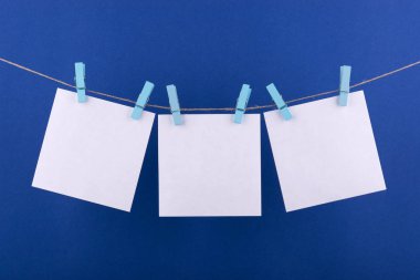 notlar ve beyaz renk hatırlatmalar için not defteri kağıt levhalar, mavi bir arka plan üzerinde bir ip üzerinde asılı dekoratif turuncu clothespins ile sabitlenmiş