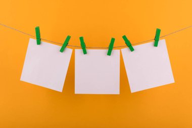 notlar ve hatırlatmalar için not defteri beyaz levhalar, dekoratif yeşil clothespins ile sabitlenmiş, turuncu bir arka plan üzerinde bir ip üzerinde asmak