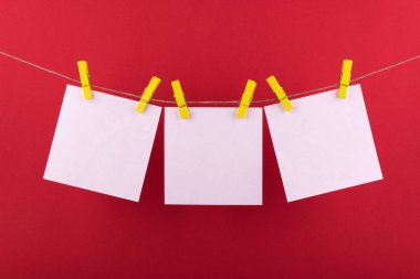 notlar ve dekoratif sarı clothespins ile sabitlenmiş beyaz renk hatırlatmalar için not defteri beyaz levhalar kırmızı bir arka plan üzerinde bir ip üzerinde asmak