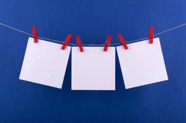 notlar ve dekoratif kırmızı clothespins ile sabitlenmiş beyaz renk hatırlatmalar için not defteri beyaz levhalar mavi bir arka plan üzerinde bir ip üzerinde asmak