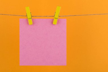 notlar ve dekoratif sarı clothespins ile sabitlenmiş pembe renk hatırlatmalar için bir not defteri kağıt levhalar turuncu bir arka plan üzerinde bir ip üzerinde asmak