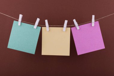yeşil, sarı ve pembe not defteri kağıt çarşaf notlar ve hatırlatmalar için, dekoratif kırmızı clothespins ile sabitlenmiş, açık yeşil bir arka plan karşı bir ip üzerinde asmak