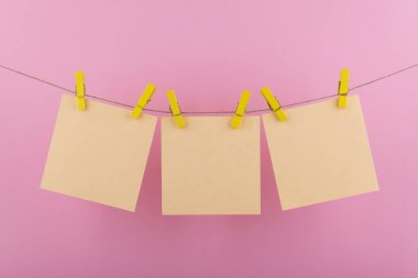 notlar ve hatırlatmalar için sarı defter kağıt levhalar, pembe bir arka plan üzerinde bir ip asılı dekoratif sarı clothespins ile sabitlenmiş