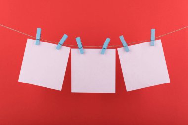 notlar ve hatırlatmalar için not defteri beyaz levhalar, dekoratif mavi clothespins ile sabitlenmiş, kırmızı bir arka plan üzerinde bir ip üzerinde asmak