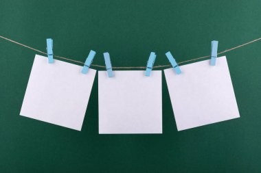 notlar ve hatırlatmalar için beyaz not defteri kağıt levhalar, dekoratif mavi clothespins ile sabitlenmiş, yeşil bir arka plan üzerinde bir ip üzerinde asmak