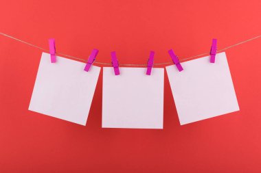 notlar ve hatırlatmalar için not defteri beyaz levhalar, dekoratif leylak clothespins ile sabitlenmiş, kırmızı bir arka plan üzerinde bir ip üzerinde asmak
