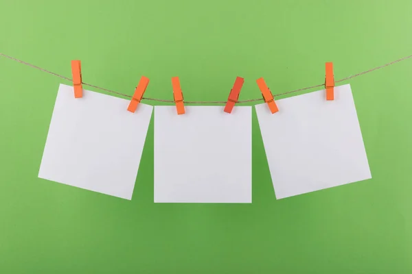 notlar ve hatırlatmalar için not defteri beyaz levhalar, dekoratif turuncu clothespins ile sabitlenmiş, açık yeşil bir arka plan üzerinde bir ip üzerinde asmak