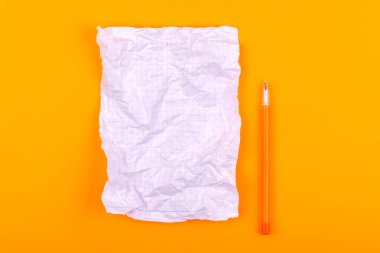 Turuncu bir arka plan üzerinde sarı bir kalemin yanında metinler, notlar ve çizimler için not defteri olan beyaz buruşturulmuş kağıt