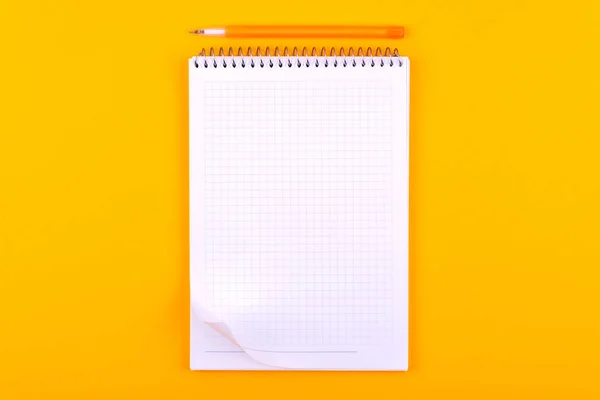 Notebook on a spring with white sheets of paper for drawings, texts and notes, next to a yellow pen lies on an orange background