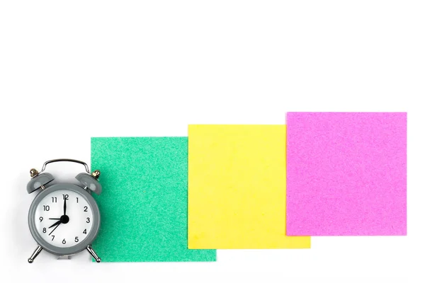 白色背景上带有闹钟的时钟躺在绿色 粉红色 黄色彩色纸叶上 用于笔记 — 图库照片