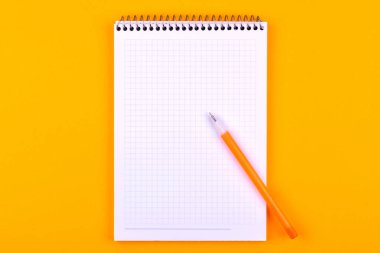 Çizimler, metinler ve notlar için beyaz kağıt yapraklı bir yay üzerinde not defteri, turuncu bir arka plan üzerinde sarı bir kalem in yanında yatıyor