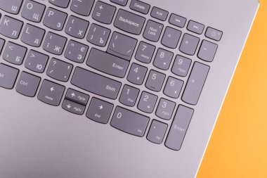 Internet'e bağlı modern klavyesi ve bilgisayar ağı olan gümüş grisi dizüstü bilgisayar, ofisteturuncu bir masaüstünde yer alır