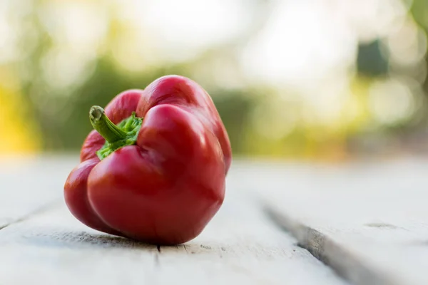 Red sweet pepper from the crop of the garden, lies on a wooden table in the open air against the background of the garden for healthy and tasty food in the form of a salad of fresh vegetables