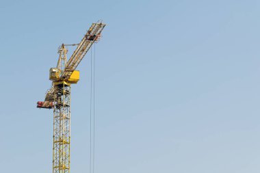 Mavi gökyüzüne karşı sarı bir yüksek katlı bina vinç bir mimari projeye göre metal, beton ve tuğla modern teknolojileri kullanarak çok katlı apartmanlar inşa