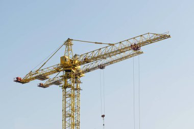 Mavi gökyüzüne karşı sarı bir yüksek katlı bina vinç bir mimari projeye göre metal, beton ve tuğla modern teknolojileri kullanarak çok katlı apartmanlar inşa