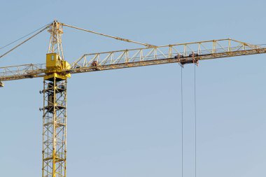 Mavi gökyüzüne karşı sarı bir yüksek katlı bina vinç bir mimari projeye göre metal, beton ve tuğla modern teknolojileri kullanarak çok katlı apartmanlar inşa