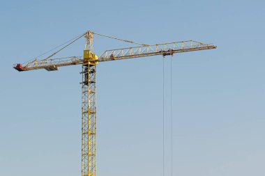 Mavi gökyüzüne karşı sarı bir yüksek katlı bina vinç bir mimari projeye göre metal, beton ve tuğla modern teknolojileri kullanarak çok katlı apartmanlar inşa