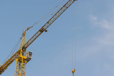 Mavi gökyüzüne karşı sarı bir yüksek katlı bina vinç bir mimari projeye göre metal, beton ve tuğla modern teknolojileri kullanarak çok katlı apartmanlar inşa