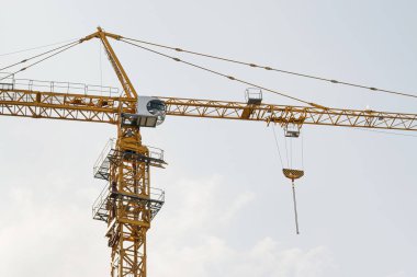 Mavi gökyüzüne karşı sarı bir yüksek katlı bina vinç bir mimari projeye göre metal, beton ve tuğla modern teknolojileri kullanarak çok katlı apartmanlar inşa