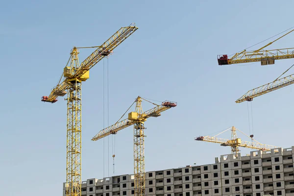 Birkaç sarı yüksek katlı inşaat vinçler mimari tasarıma göre metal, beton ve tuğla modern teknolojileri kullanarak çok katlı çok katlı konut binaları inşa