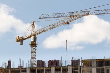 Mavi gökyüzüne karşı sarı bir yüksek katlı bina vinç bir mimari projeye göre metal, beton ve tuğla modern teknolojileri kullanarak çok katlı apartmanlar inşa