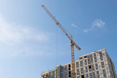 Mavi gökyüzüne karşı sarı bir yüksek katlı bina vinç bir mimari projeye göre metal, beton ve tuğla modern teknolojileri kullanarak çok katlı apartmanlar inşa