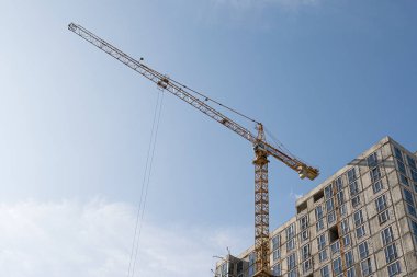 Mavi gökyüzüne karşı sarı bir yüksek katlı bina vinç bir mimari projeye göre metal, beton ve tuğla modern teknolojileri kullanarak çok katlı apartmanlar inşa