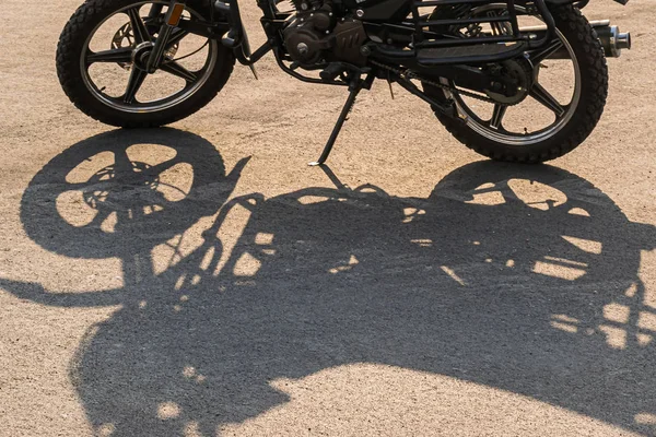 Siyah motosiklet güneşin altındaki kaldırıma park edilmiş.
