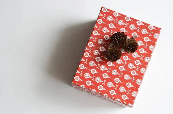 休日のギフトボックス クリスマスと新年のためのホリデーボックス 白い模様の赤い箱と白い背景のモミのコーン 休日の贈り物 お祝いの準備 — ストック写真