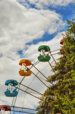 Şehir parkında dönme dolap. yeşil ağaç, ladin ve mavi gökyüzü beyaz bulutlarla.