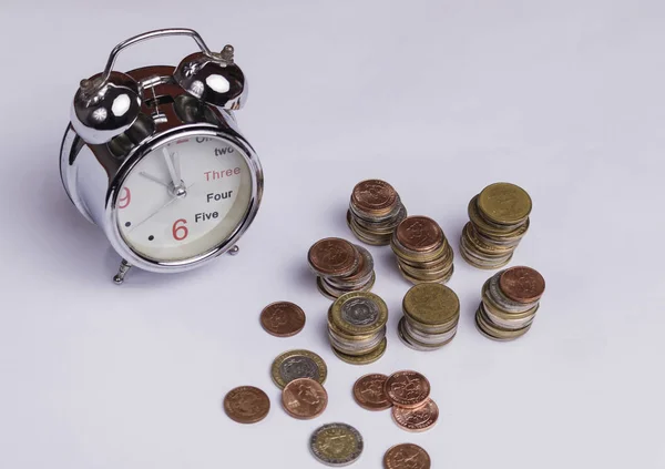 money in the form of coins, old clock with bells, a black calculator and dice set, on white surface