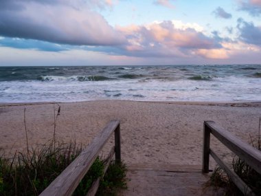 St. Augustine, Florida 'daki Atlantik Okyanusu' nun kumlu sahiline giden tahta tahta kaldırım. Gün batımından hemen önce dalgaların üzerinde bulutlu bir gökyüzü vardı..