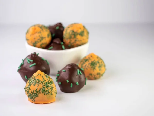 Carrot cake balls and chocolate mint cake balls with sprinkles sitting in a white brown and in front of it on a white surface.