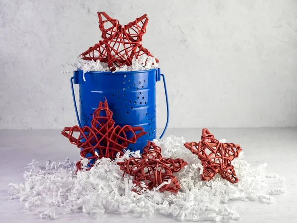 Red and blue wooden stars set on a bed of white paper shreds with a plaster background for 4th of July, Memorial Day.
