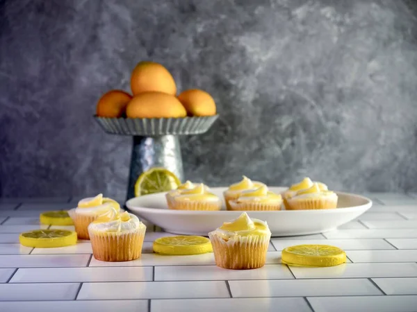 Mini lemon cupcakes with a rustic metal display filled with artificial lemons and artificial lemon slices arranged between the cupcakes.  Delicious dessert with citrus fruit.