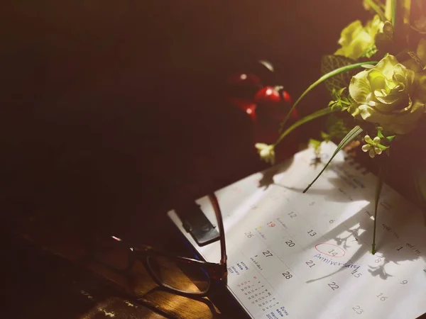 Çiçek buketi, kırmızı çalar saat ve gözlük, takvim, uyarı mektubu Anniversary.Valentines günü, 14 Şubat için boş eski ahşap plakalar üzerinde yazılı. Rustik natürmort ve koyu arka plan, loş ışık.