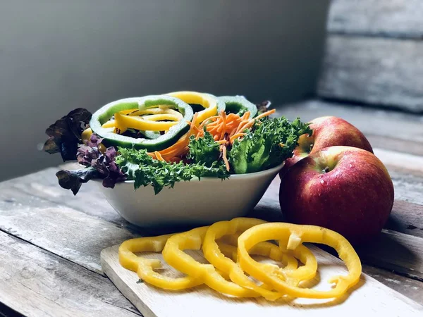 Delicious vegetable salad.Yellow and green sweet pepper,Green Oak lettuce,Red Oak lettuce,sliced carrots,and fresh apple on old wood planks,with lens flare.Rustic still life.Healthy food concept.